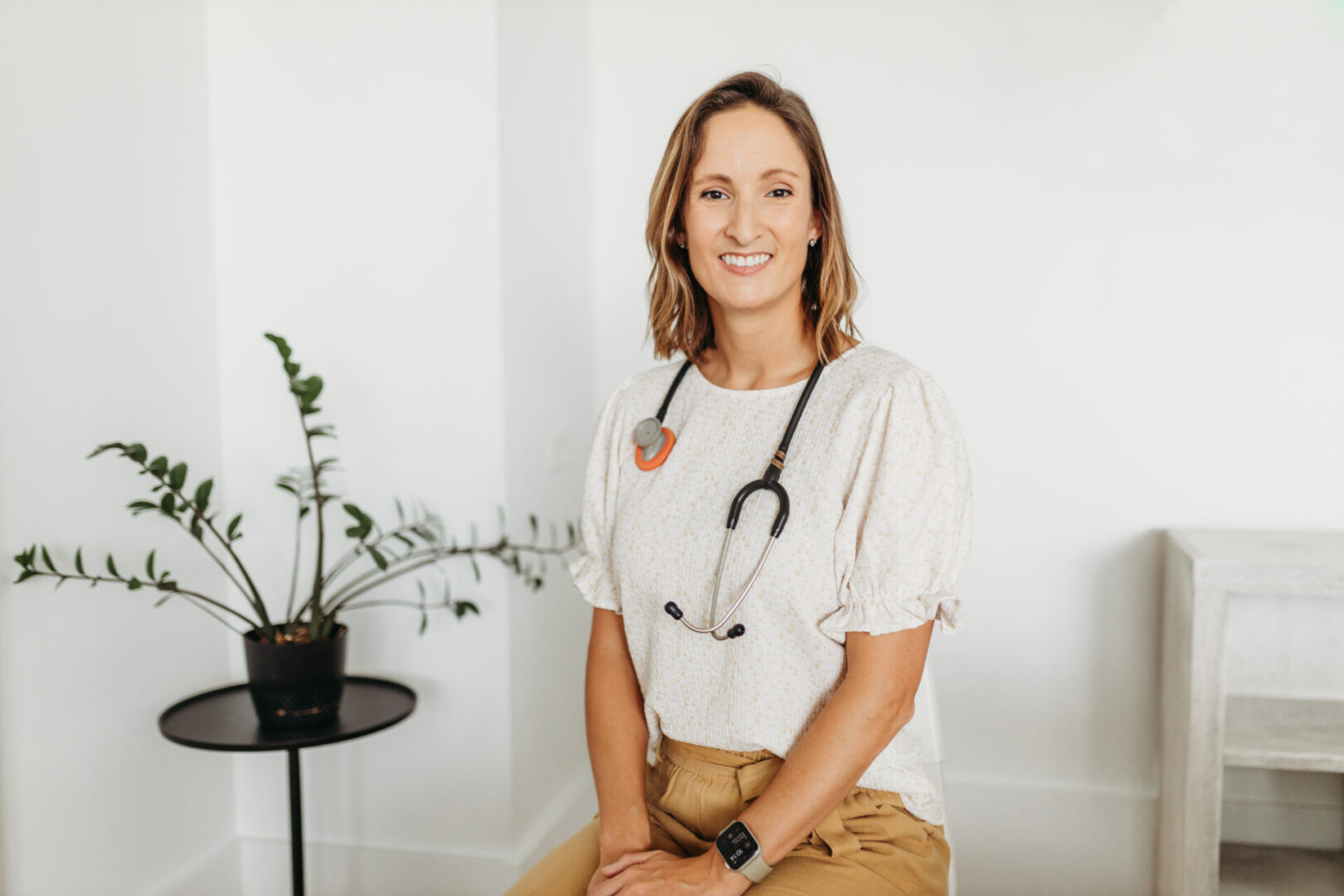 A woman sitting in front of a plant wearing a stethoscope.