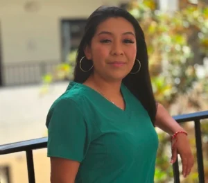 Woman in teal scrubs smiling by railing
